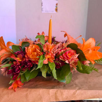 Orange and pink floral centerpiece with a tall candle in the middle