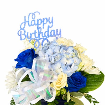Blue and cream floral arrangement in a dark vase with a Happy Birthday topper