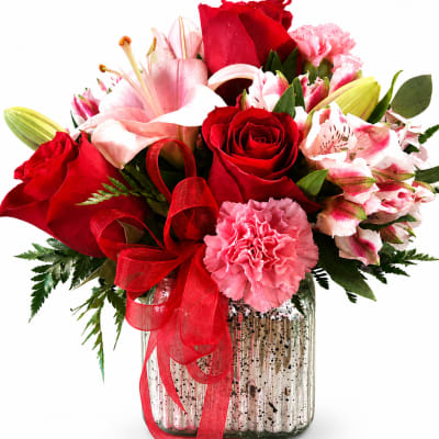 Red roses and pink lilies in a glass vase with a red ribbon