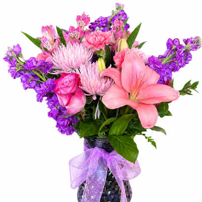 Pink and purple mixed bouquet in a dark vase with a lavender ribbon