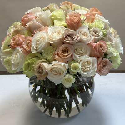 Bouquet of cream, blush, and pale green roses in a round glass vase