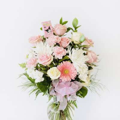 Pink and white mixed flower arrangement in a glass vase with a pink ribbon