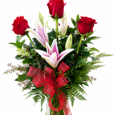 Red roses and pink lilies in a glass vase with a red ribbon