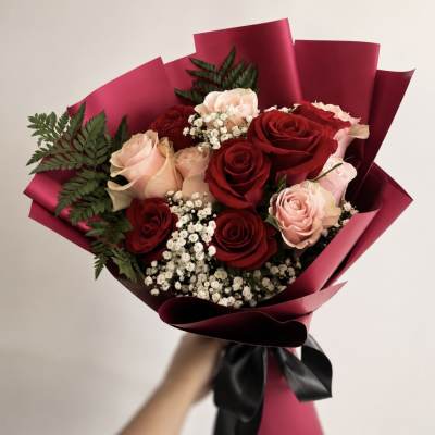 Handheld bouquet of red and blush roses wrapped in burgundy paper