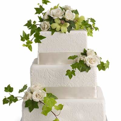 Three-tier white cake decorated with white roses and green orchids cascading with ivy