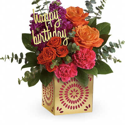 Birthday flower arrangement with orange roses, pink carnations, and purple blooms in a gold cube vase