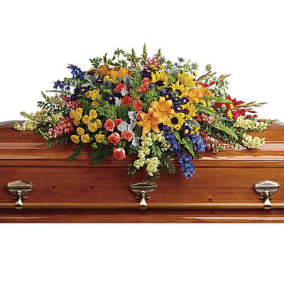 Large multicolor casket spray of lilies, roses, delphinium, and mixed flowers on a wooden casket