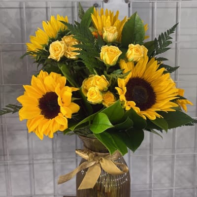 Yellow sunflowers and roses arranged in a glass vase with a ribbon