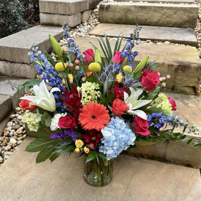 Colorful mixed bouquet in a glass vase with lilies, roses, hydrangea, and blue delphinium