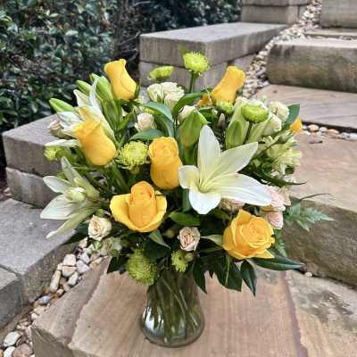 Yellow roses and white lilies arranged in a clear glass vase