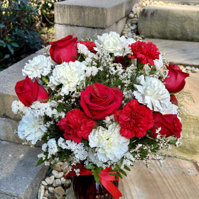 Bouquet of red roses and white and red carnations in a dark vase