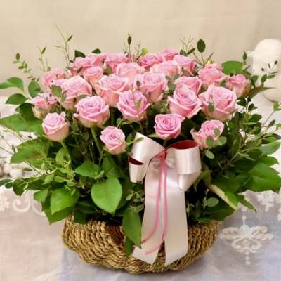Pink roses arranged in a woven basket with a ribbon bow