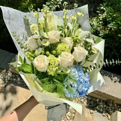 Bouquet of white roses, blue hydrangea, and green accents wrapped in paper