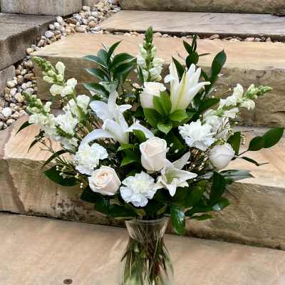 White lilies and roses arranged in a clear glass vase