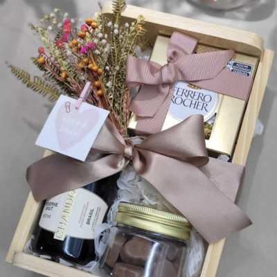 Gift box with dried flowers, chocolates, and a bottle of wine tied with pink ribbon