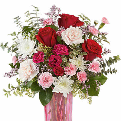 Arrangement of red roses, pink carnations, and white mums in a tall pink glass vase