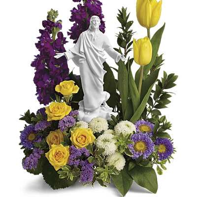 Religious floral arrangement with yellow roses, tulips and purple flowers around a white Jesus figurine
