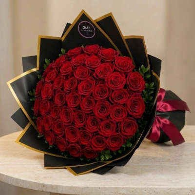 Large bouquet of red roses wrapped in black paper with gold trim and a burgundy ribbon.
