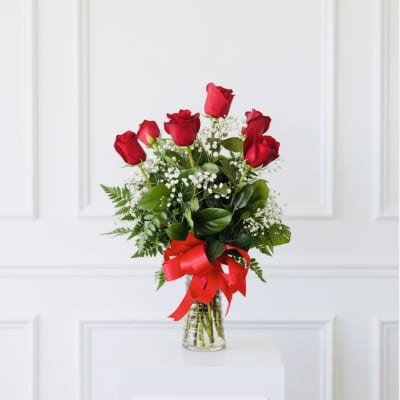 Red roses in a clear glass vase with a red ribbon