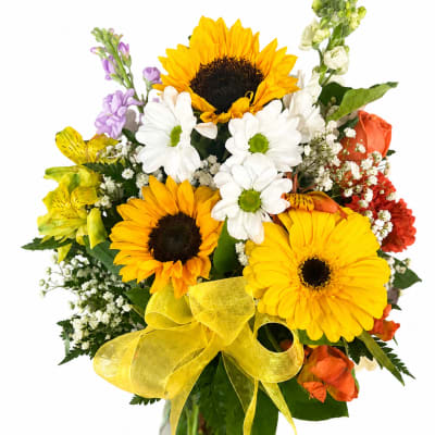 Bouquet of sunflowers, daisies, and mixed blooms in a glass vase with a yellow ribbon