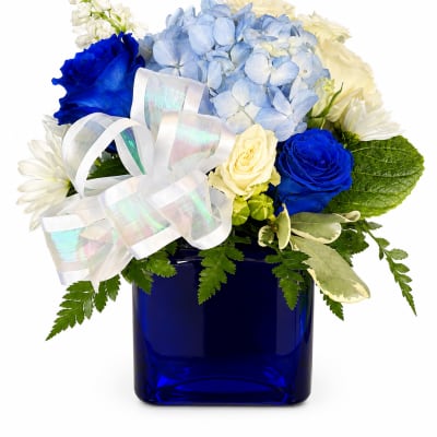 Blue and white flower arrangement in a cobalt vase with a white ribbon