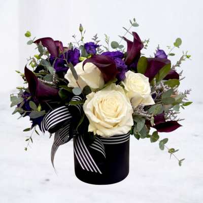 Bouquet of white roses, purple flowers, and dark calla lilies in a black vase