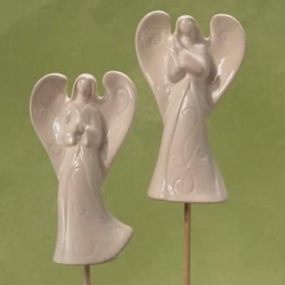 Two white ceramic angel ornaments on sticks against a green background