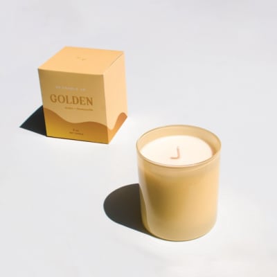 Gold candle in a glass jar beside its box