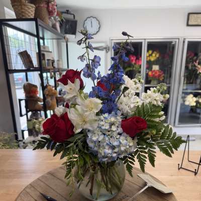 Mixed bouquet with red roses, blue delphinium, white alstroemeria, and hydrangea in a glass vase
