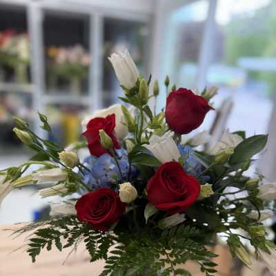 Bouquet of red roses, white bellflowers, and blue hydrangeas in a glass vase