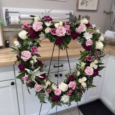 Heart-shaped floral wreath with pink and white roses on a stand