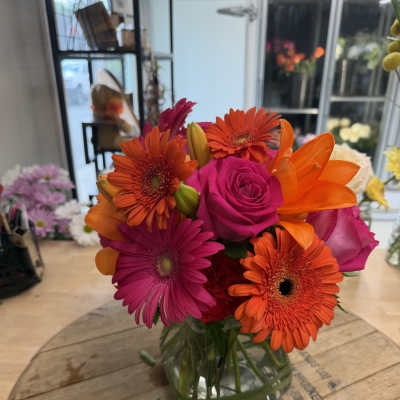 Bright mixed bouquet of pink roses, orange gerberas, and lilies in a glass vase