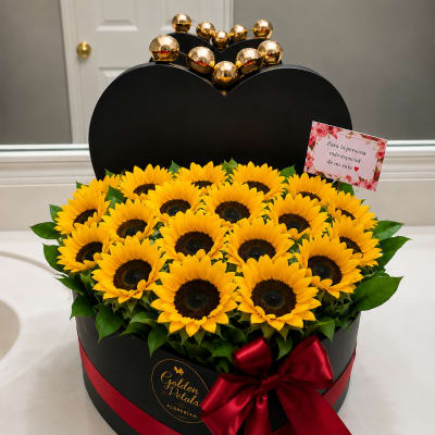 Heart-shaped box of yellow sunflowers with a red ribbon and gold topper