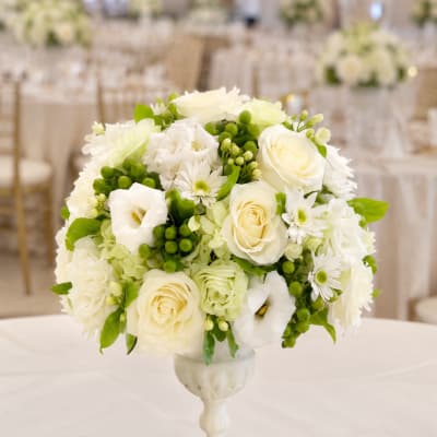White floral arrangement in a pedestal vase with green accents