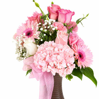 Pink roses and gerbera daisies in a brown vase with a pink ribbon