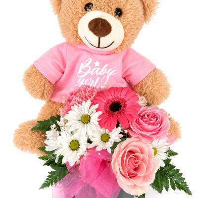 Teddy bear in a pink shirt holding pink and white flowers in a box