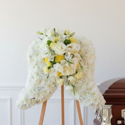 White floral funeral spray on a wooden easel beside a casket