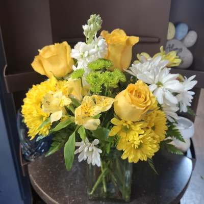 Yellow roses and white daisies arranged in a clear glass vase
