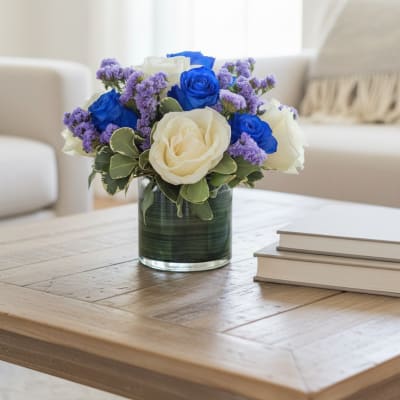 Blue and white roses in a glass vase with purple filler flowers