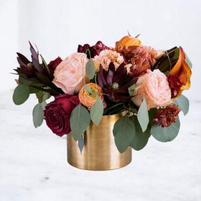 Bouquet of peach and burgundy flowers in a gold vase