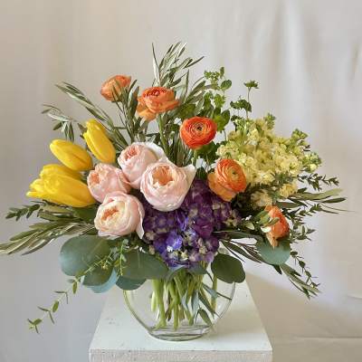 Mixed bouquet of yellow tulips, peach ranunculus, and purple hydrangea in a glass vase