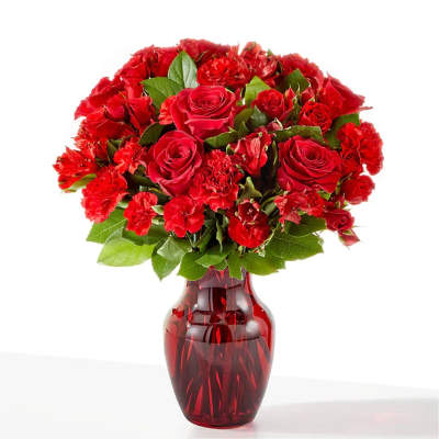 Red roses and carnations arranged in a red glass vase