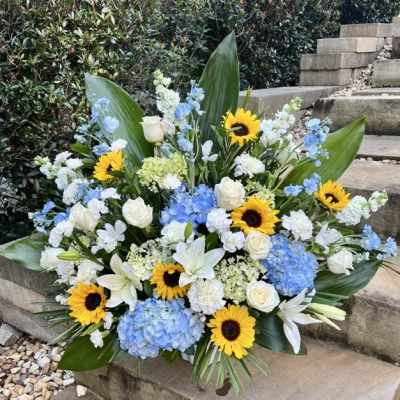 Large floral arrangement with sunflowers, white roses, blue hydrangeas, and white lilies