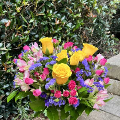 Bouquet of yellow roses, pink alstroemeria, and purple filler in a glass vase
