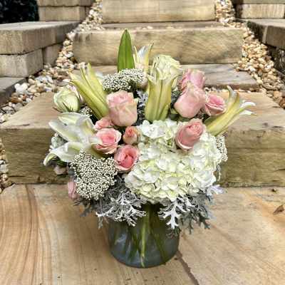 Pink roses and white lilies arranged in a glass vase with white hydrangeas