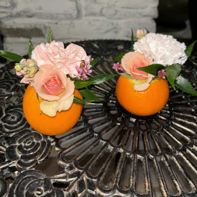 Two small floral arrangements in orange halves on a table