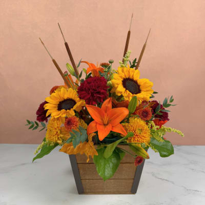 Autumn flower arrangement with sunflowers, lilies, and mums in a wooden planter