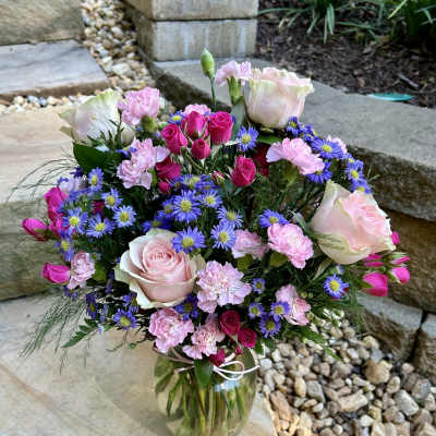 Bouquet of pink roses, carnations, and purple daisies in a glass vase