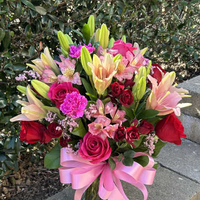 Bouquet of pink and red roses with lilies in a glass vase and pink ribbon