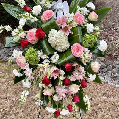 Standing floral spray with pink and red roses, white blooms, and an angel figurine